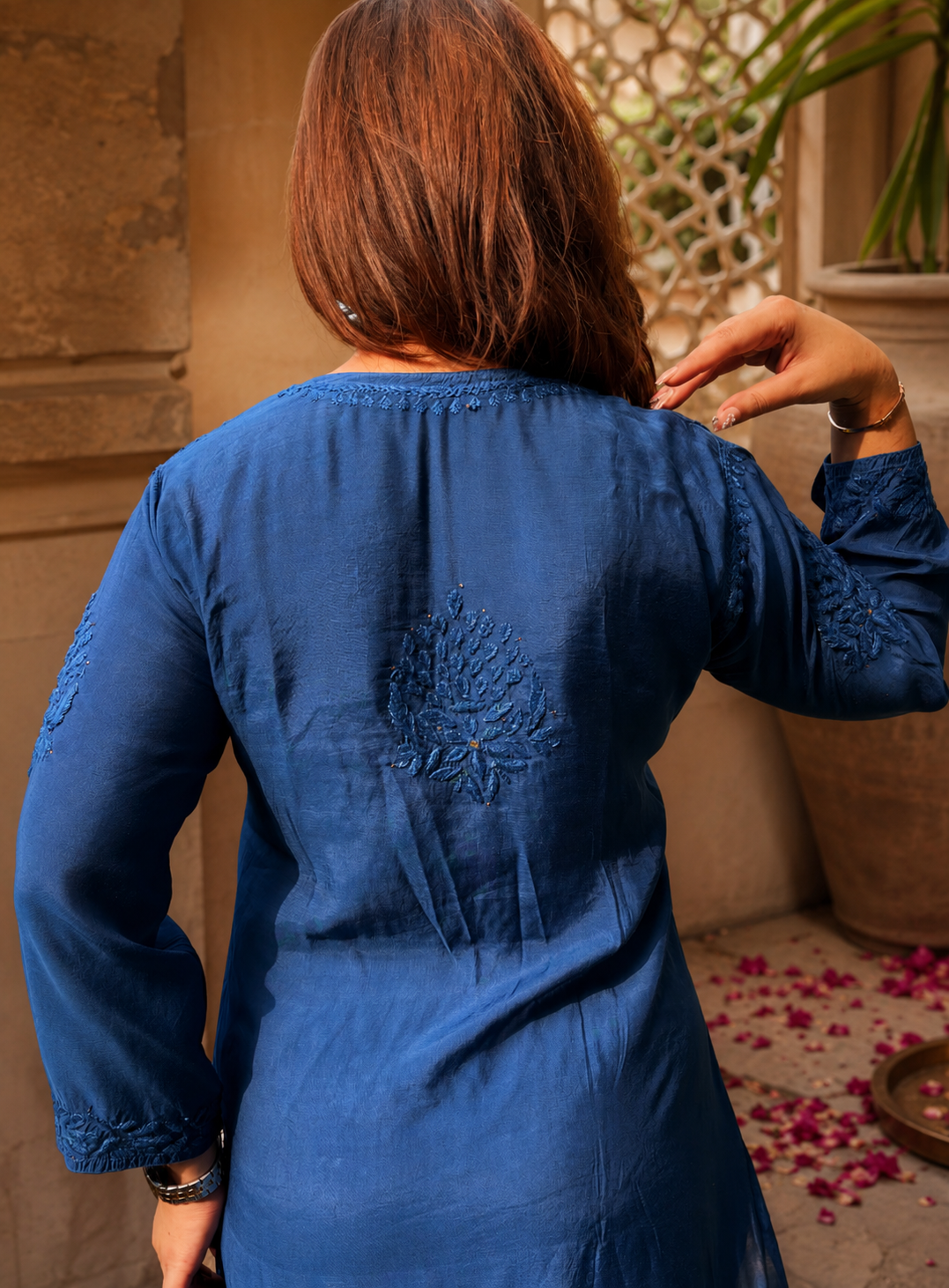 Woman wearing a blue dress with intricate detailing, standing in a decorative indoor setting.