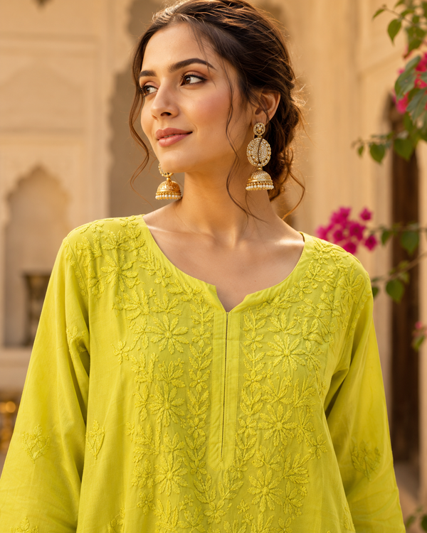 Woman wearing a bright green embroidered top with traditional earrings, standing outdoors.
