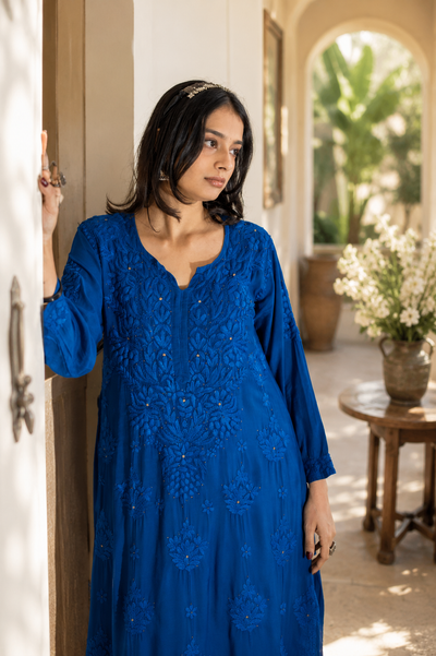 Woman wearing a blue dress with intricate patterns in an outdoor setting.