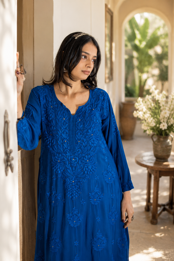 Woman wearing a blue dress with intricate patterns in an outdoor setting.