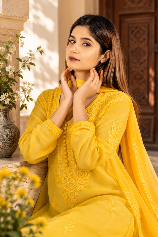 Woman in a yellow Chikankari Kurta Set outfit with floral embroidery, sitting outdoors.