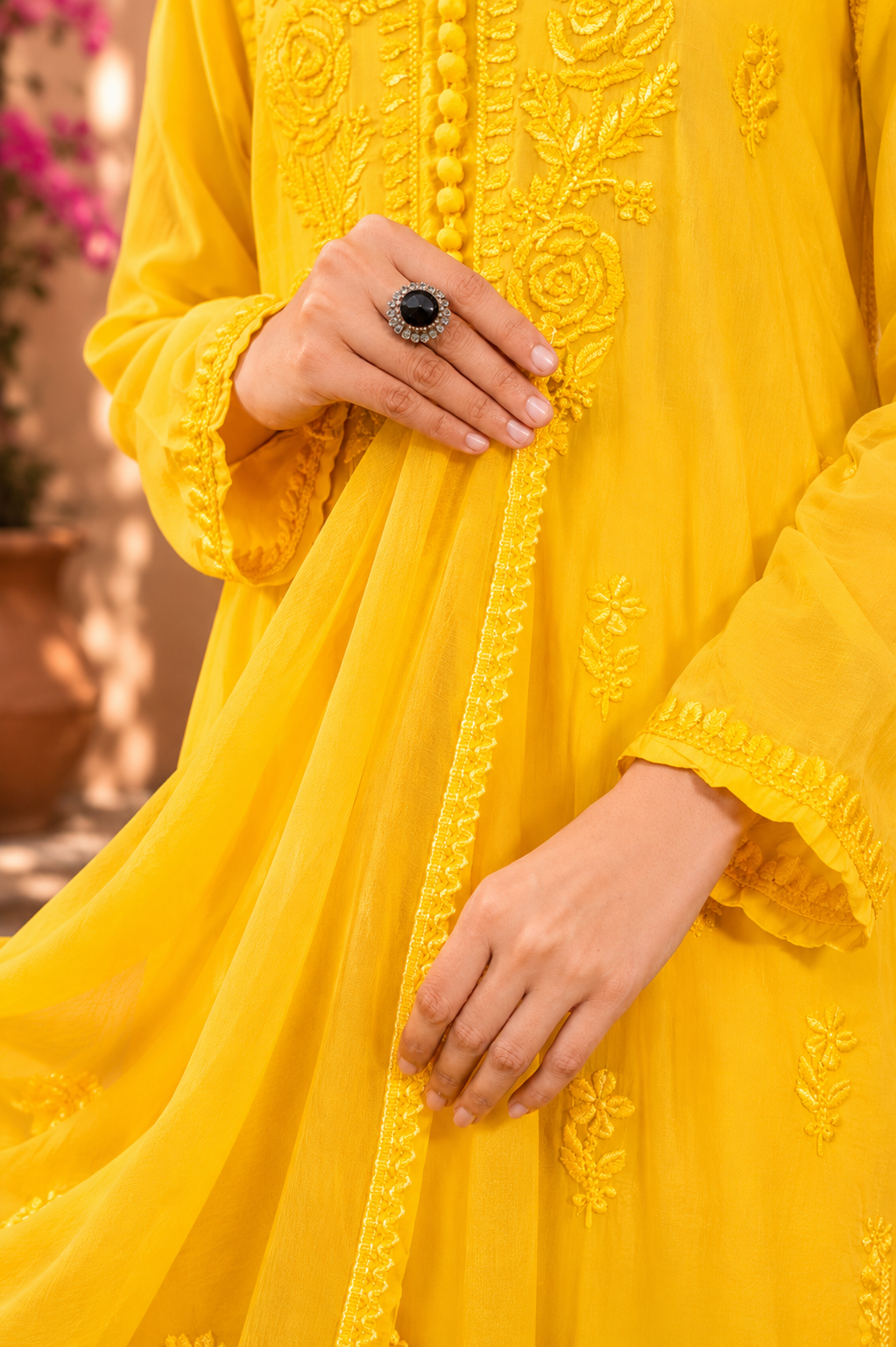 Yellow embroidered dress with a close-up of hands wearing rings.
