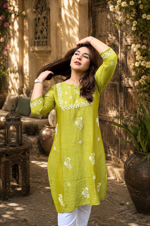 Woman in a green embroidered kurta standing outdoors with decorative elements.