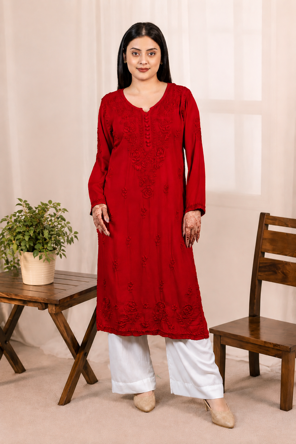 Woman wearing a red Modal kurta with white pants standing in a room with a wooden chair and table.