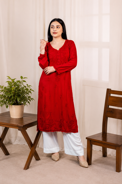 Woman wearing a red Modal kurta with white pants standing in a room with a wooden chair and table.