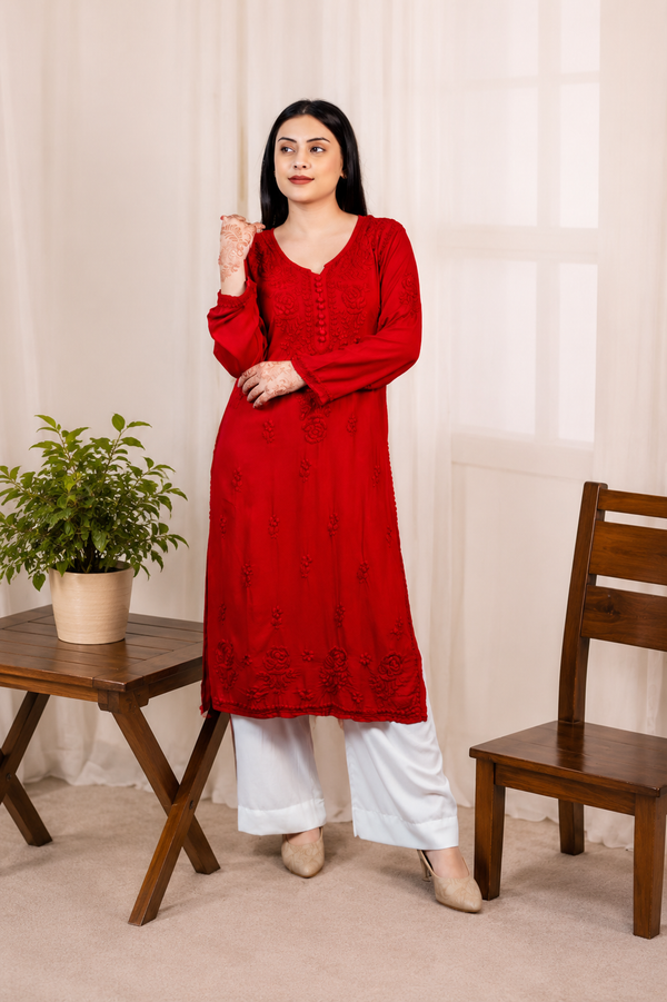 Woman wearing a red Modal kurta with white pants standing in a room with a wooden chair and table.