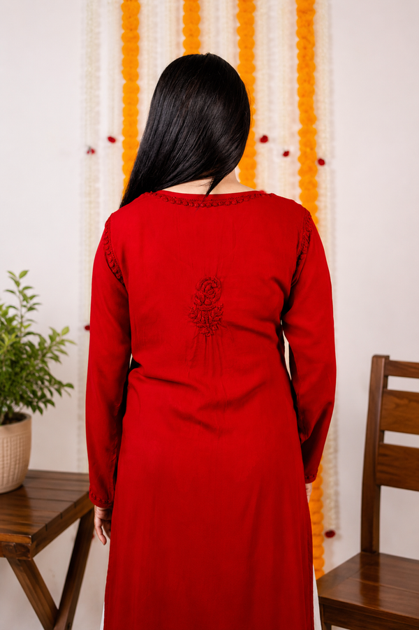 Person wearing a red  Modal Chikankari Kurta with a decorative pattern in a room with a plant and chair.
