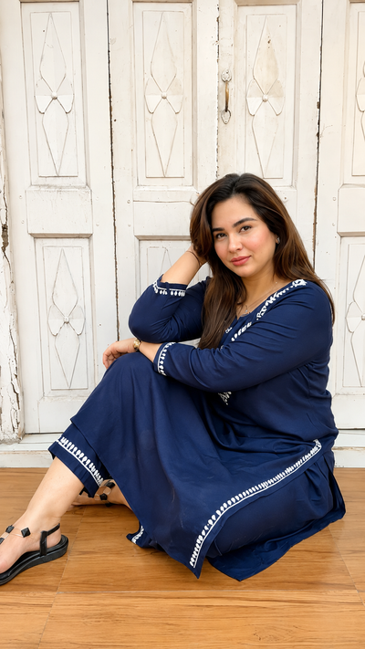 Woman in a blue dress sitting on a wooden floor with a white wooden door in the background