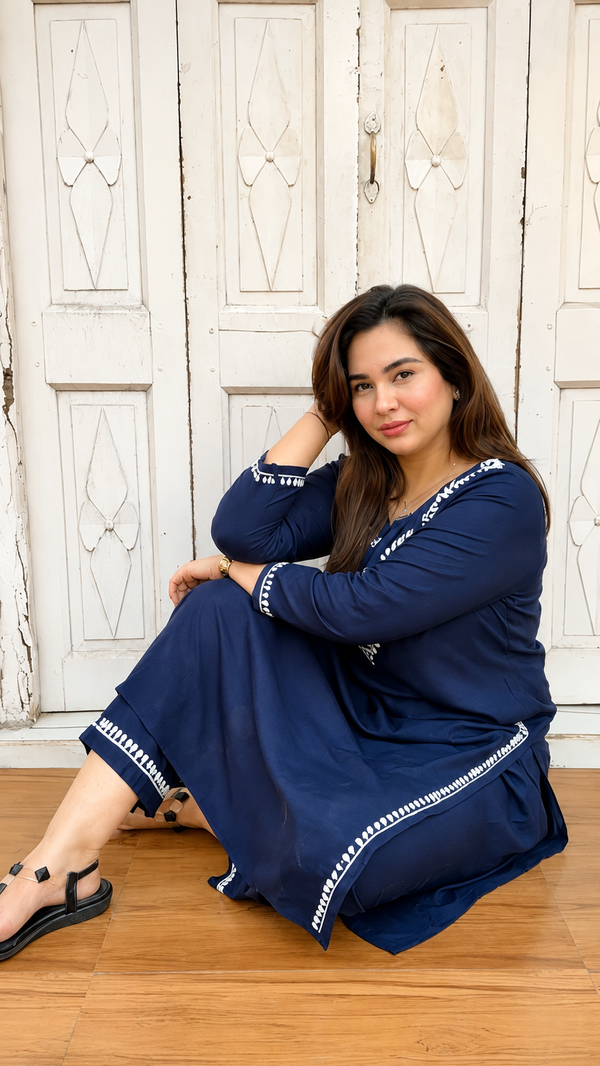 Woman in a blue dress sitting on a wooden floor with a white wooden door in the background