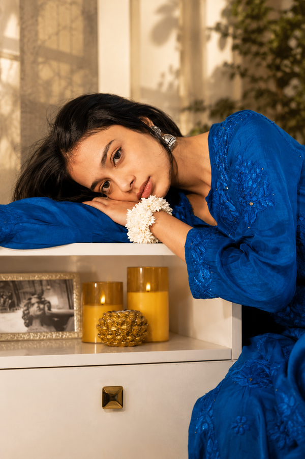 Woman in a blue dress leaning on a shelf with candles and decor
