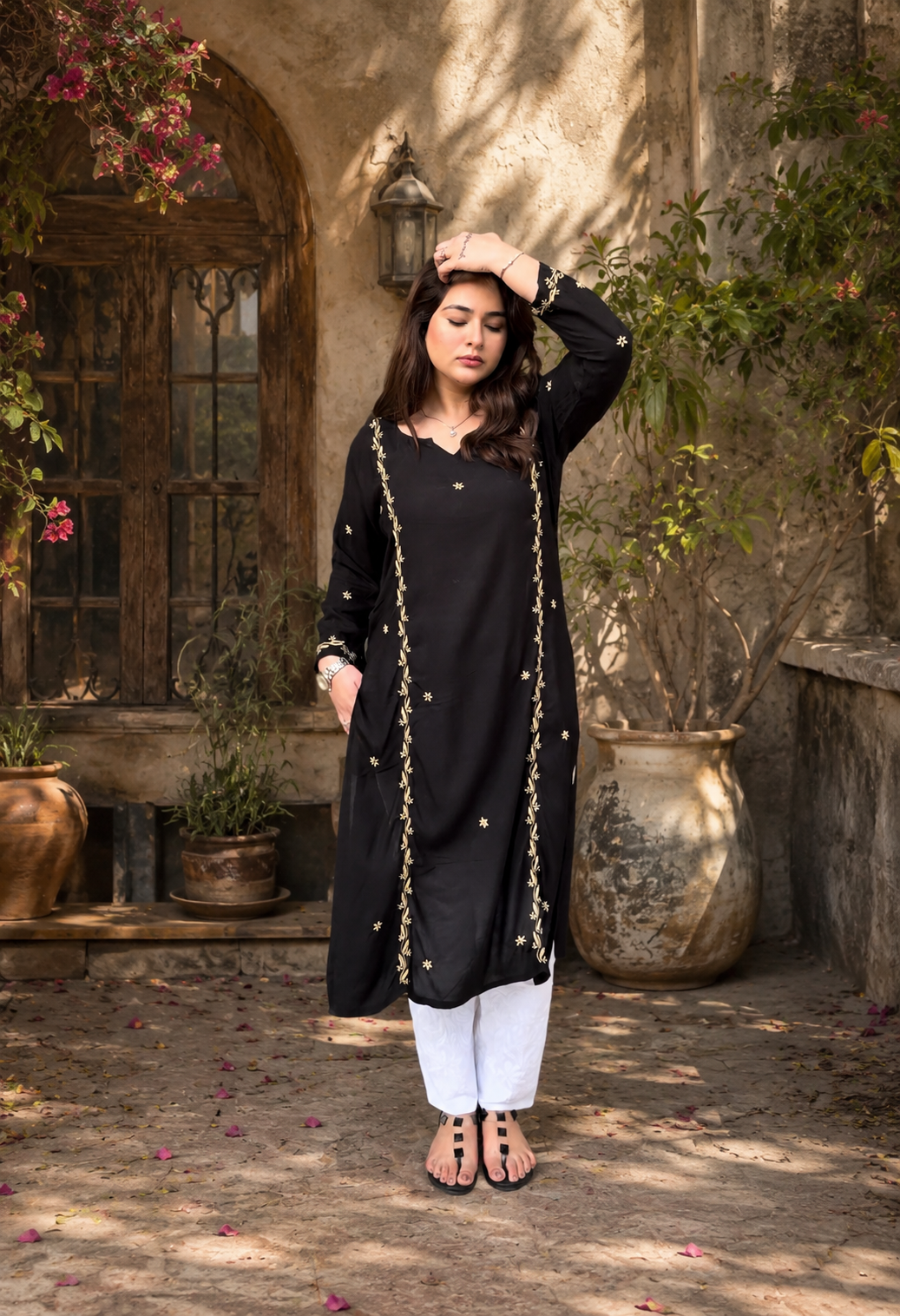 Woman in a Black Chikankari and white outfit standing in an outdoor setting with plants and stone walls.