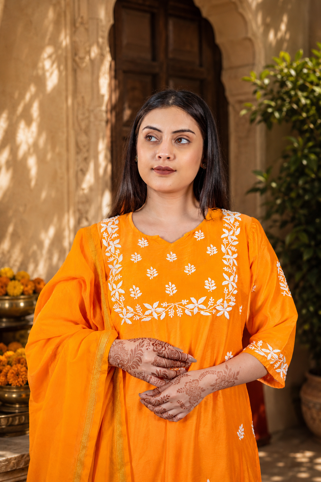 Woman in an orange traditional outfit with white patterns standing outdoors.