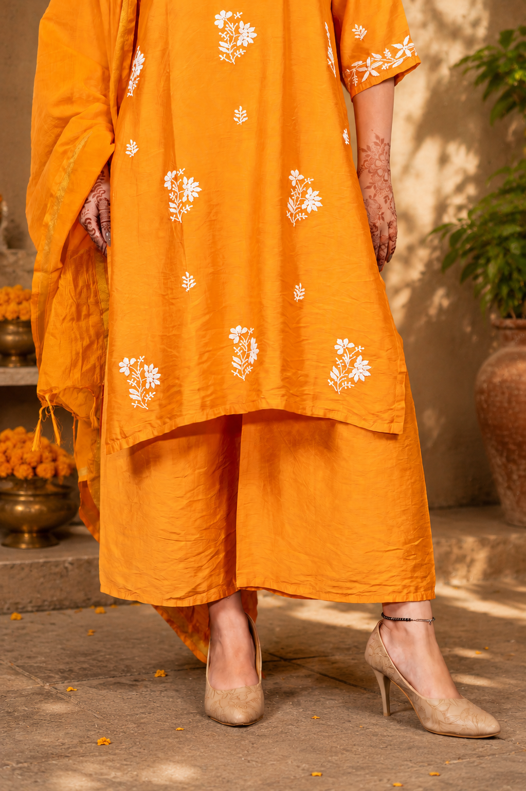 Person wearing an orange traditional outfit with white floral patterns, standing outdoors.
